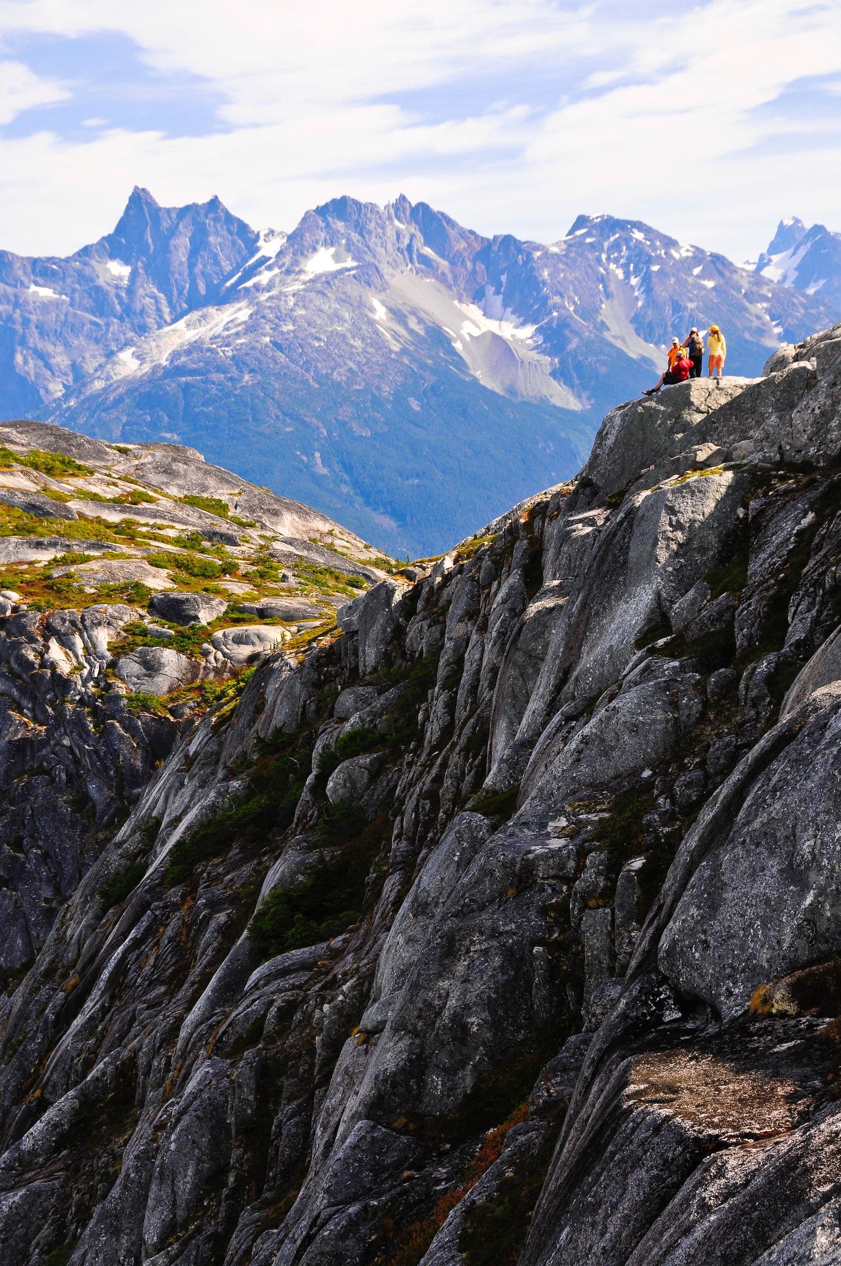 A group of people sitting on the ledge of a mountain looking out at the view